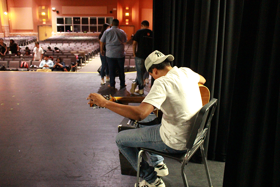 Junior Omar Tello Gonzales tunning his guitar before Cinco De Mayo while others are on the stage practicing their acts. Gonzales played classical Mariachi music to represent the Mexican culture.