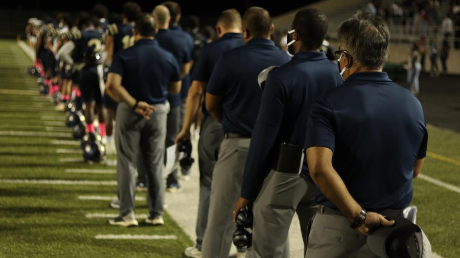 Looking towards the future- Head Coach Humberto, Garza  (middle right) pauses for anthem with students and coaches at Akins first homecoming game against Del Valle.