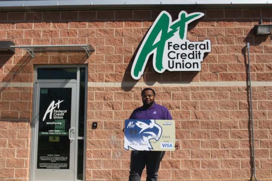Nathan Willis, assistant branch manager of the A+FCU branch at Akins poses with a prop debit card by the A+FCU building. Willis wants Akins students to know about scams students have fallen for.