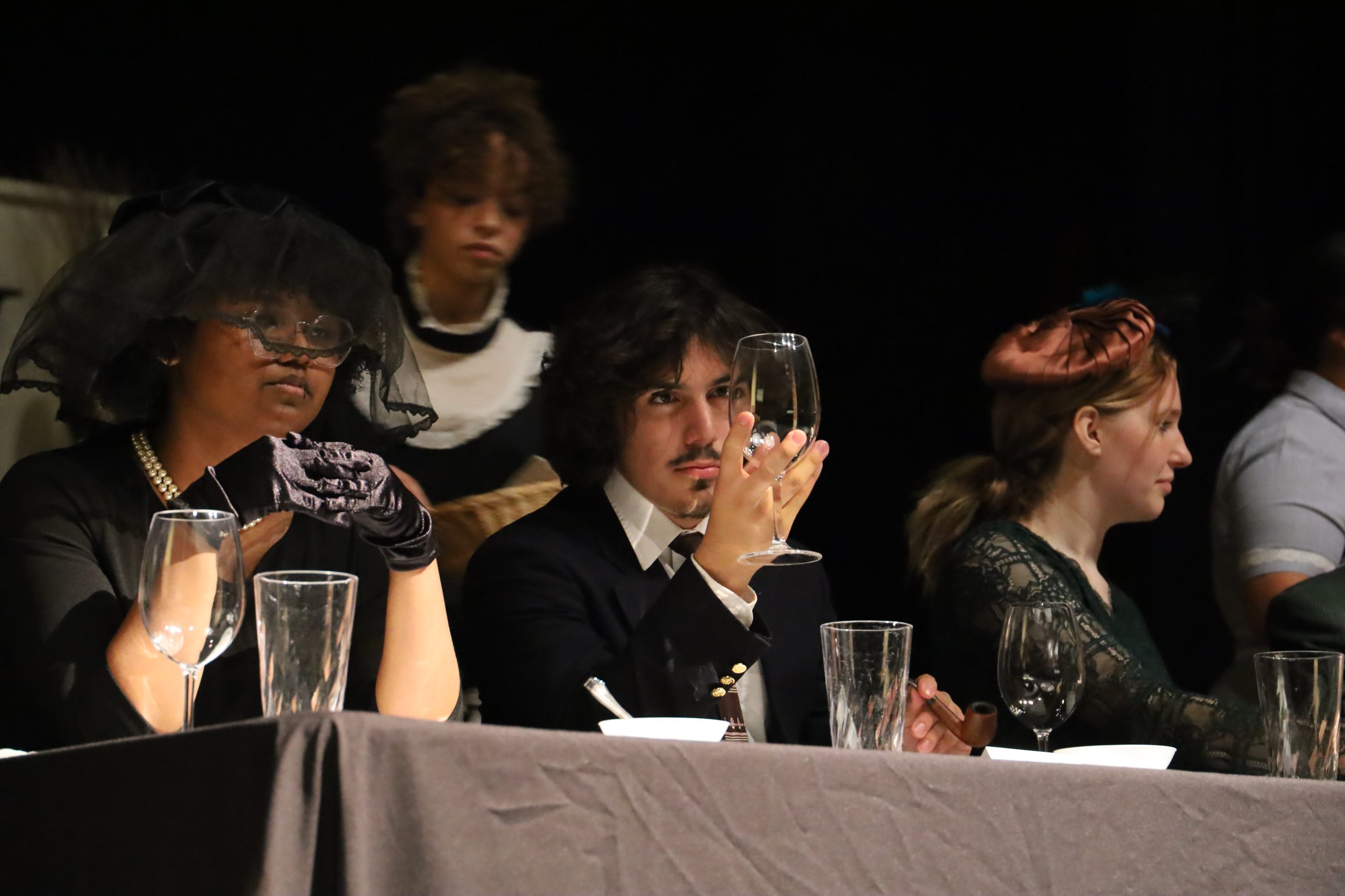 Senior Joaquin Arredondo who plays Professor Plum examines a glass while waiting to be served food with senior Q Perry who plays Ms. White.