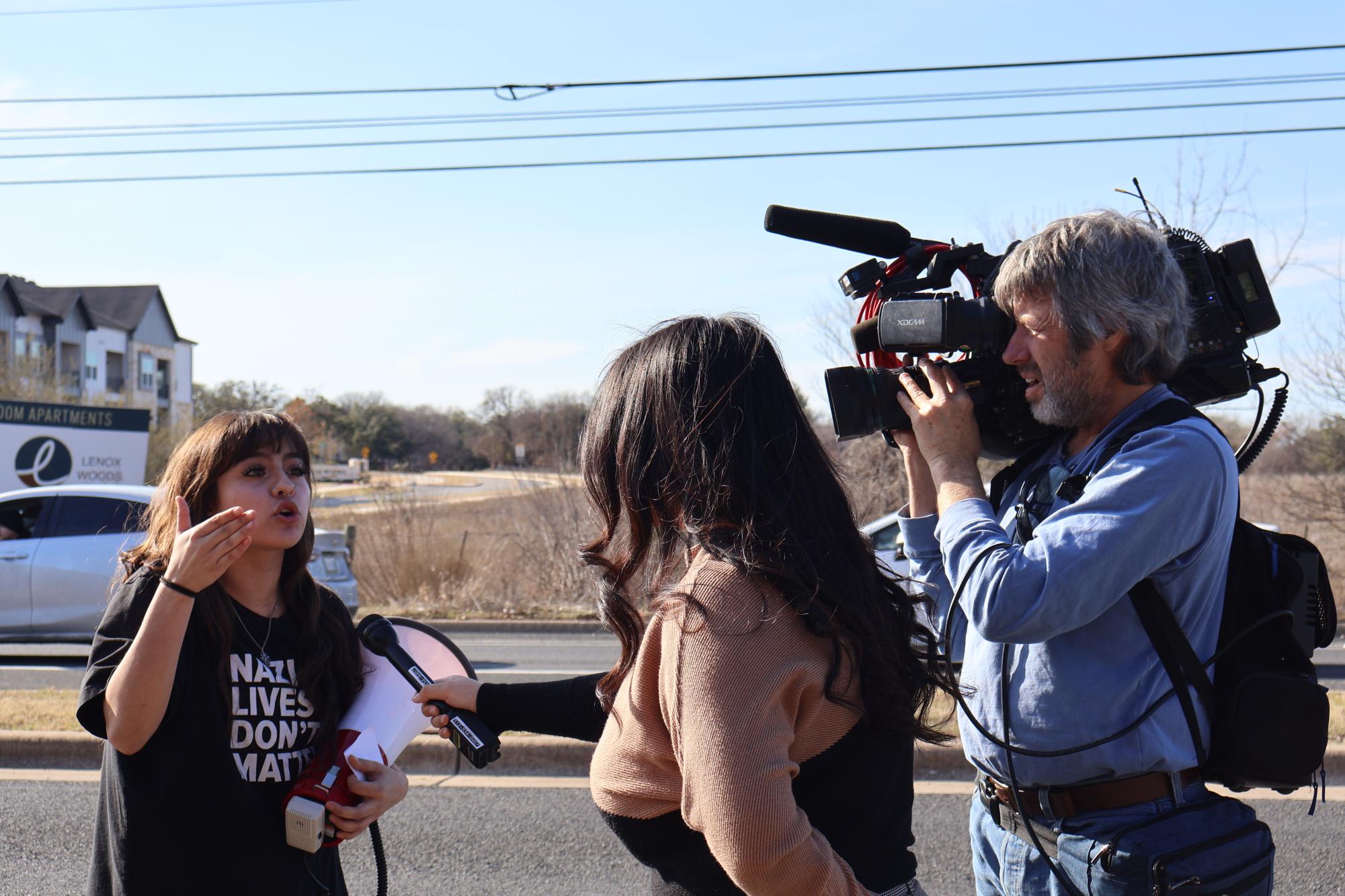 Senior Adeleah Cardenas answers questions from a reporter from the KVUE television station who arrived during the protest to interview students and take video of the walkout organized by students. Cardenas and several other seniors organized and promoted the protest against recent actions by ICE.